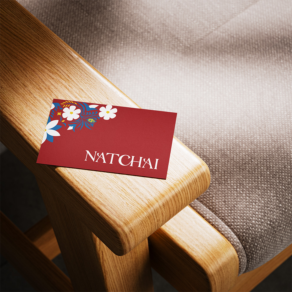 Carte de visite Natchai posée sur accoudoir en bois, fond textile
